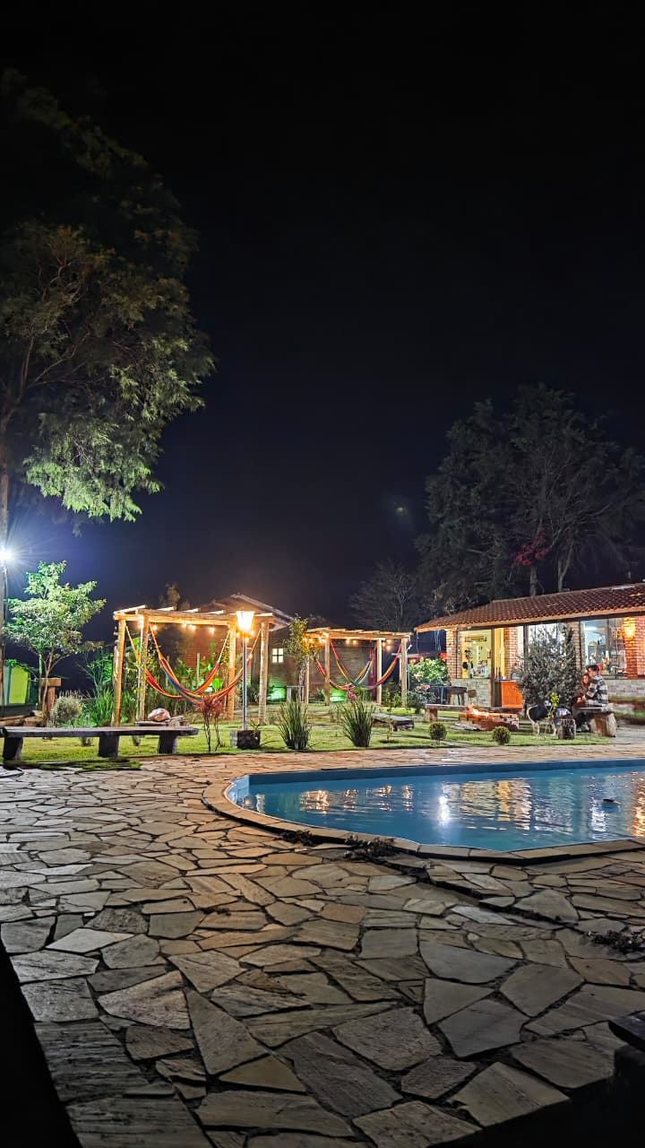 Piscina iluminada à noite com as redes e o pergolado ao fundo